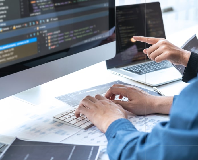 プログラムコードを表示するモニターを見ながら議論するエンジニア